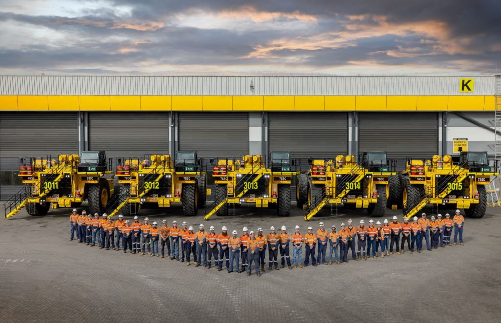 group of people wearing high vis standing in the 'v' formation infront of 5 large trucks